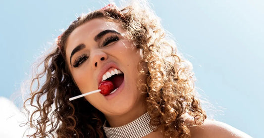 At-home lashes highlighted on a woman with curly hair enjoying a red lollipop under bright daylight