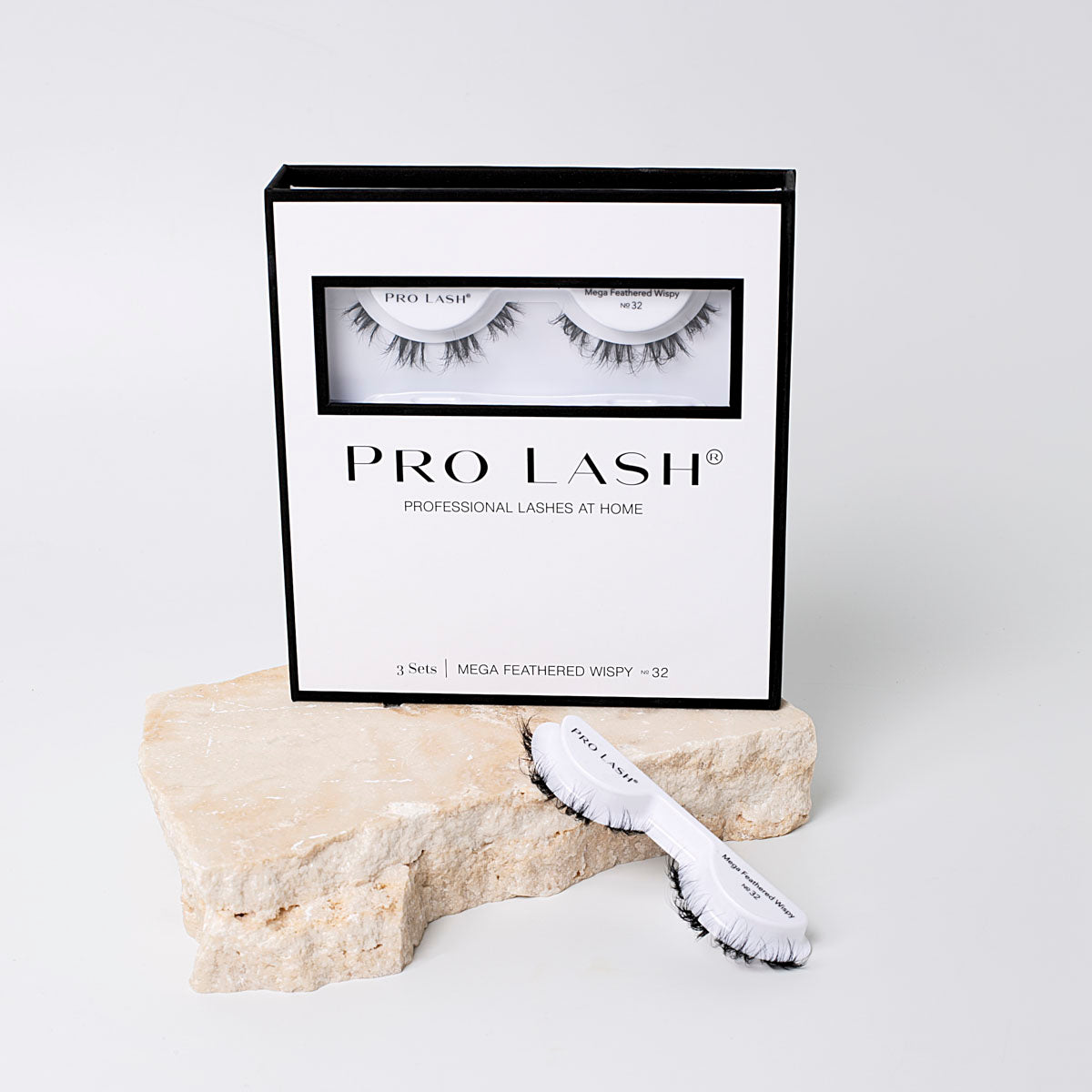 Fluffy eyelash extensions in Pro Lash Mega Feathered Wispy No.32 3-set pack, displayed in sleek black and white packaging with lash tray on stone prop