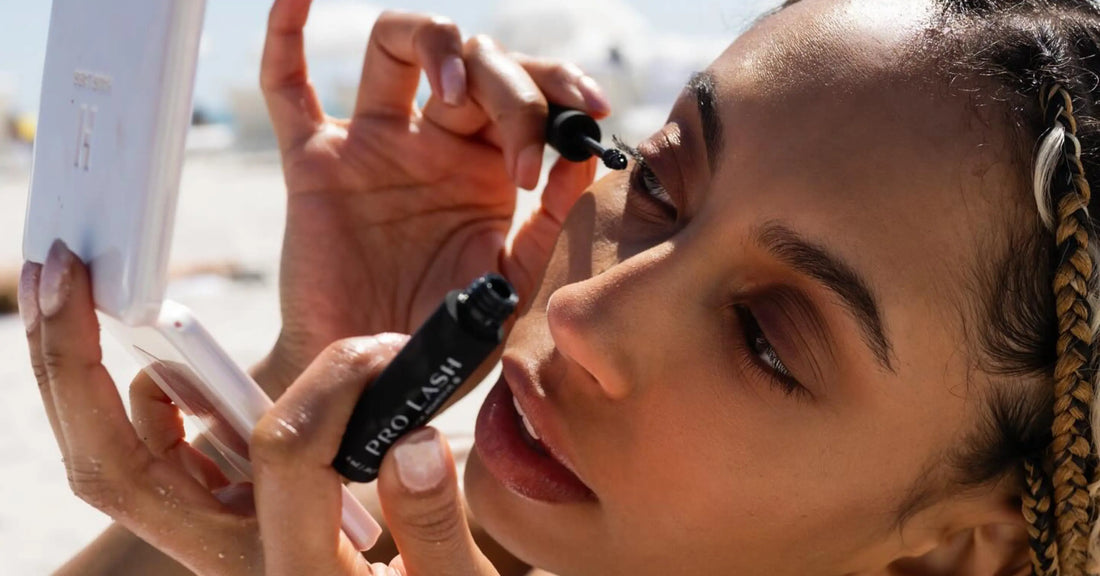 Healthy lash habits demonstrated by a model applying Pro Lash adhesive carefully while using a compact mirror outdoors.