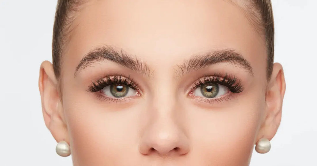 Mega eyelashes on a woman with defined brows and green eyes looking straight ahead.