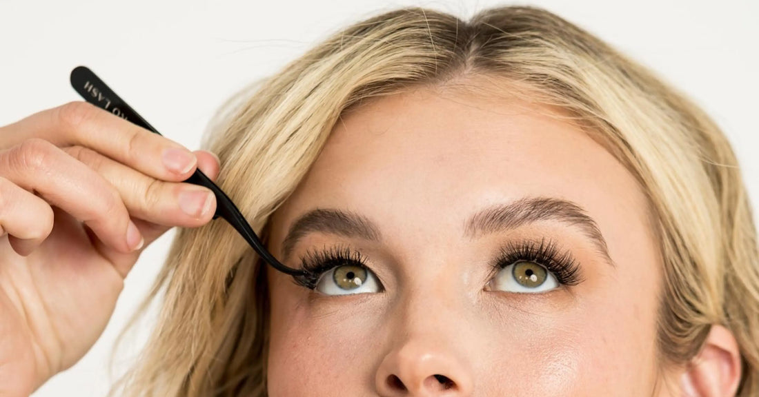 Natural volume lash extensions featured on a blonde model applying lashes with tweezers for soft, full enhancement.