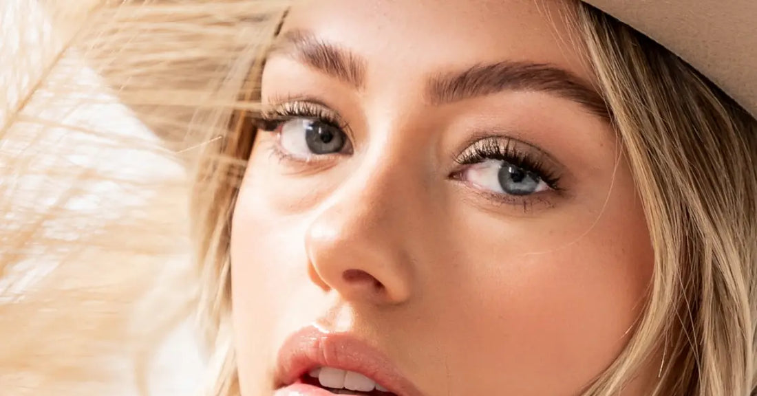 Soft natural lashes on a woman with minimal makeup and light blonde hair wearing a beige hat.