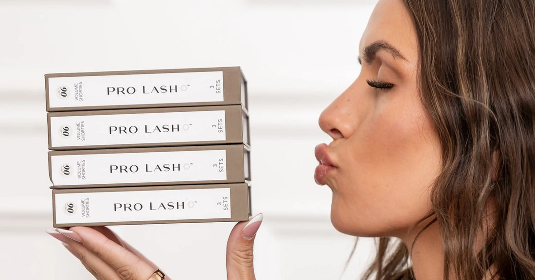 Volume lash extensions displayed as a model kisses stacked Pro Lash boxes, highlighting full, dramatic lash styles.