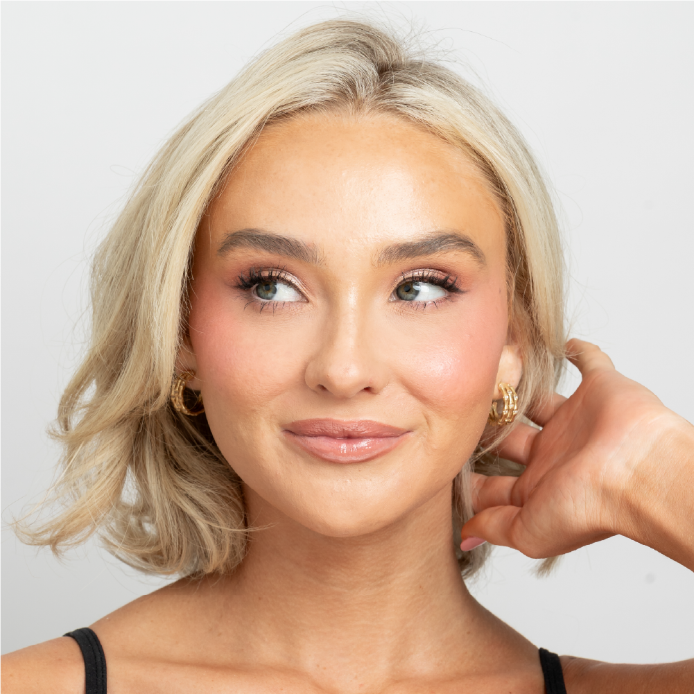 Woman with styled blonde hair and makeup against a plain background