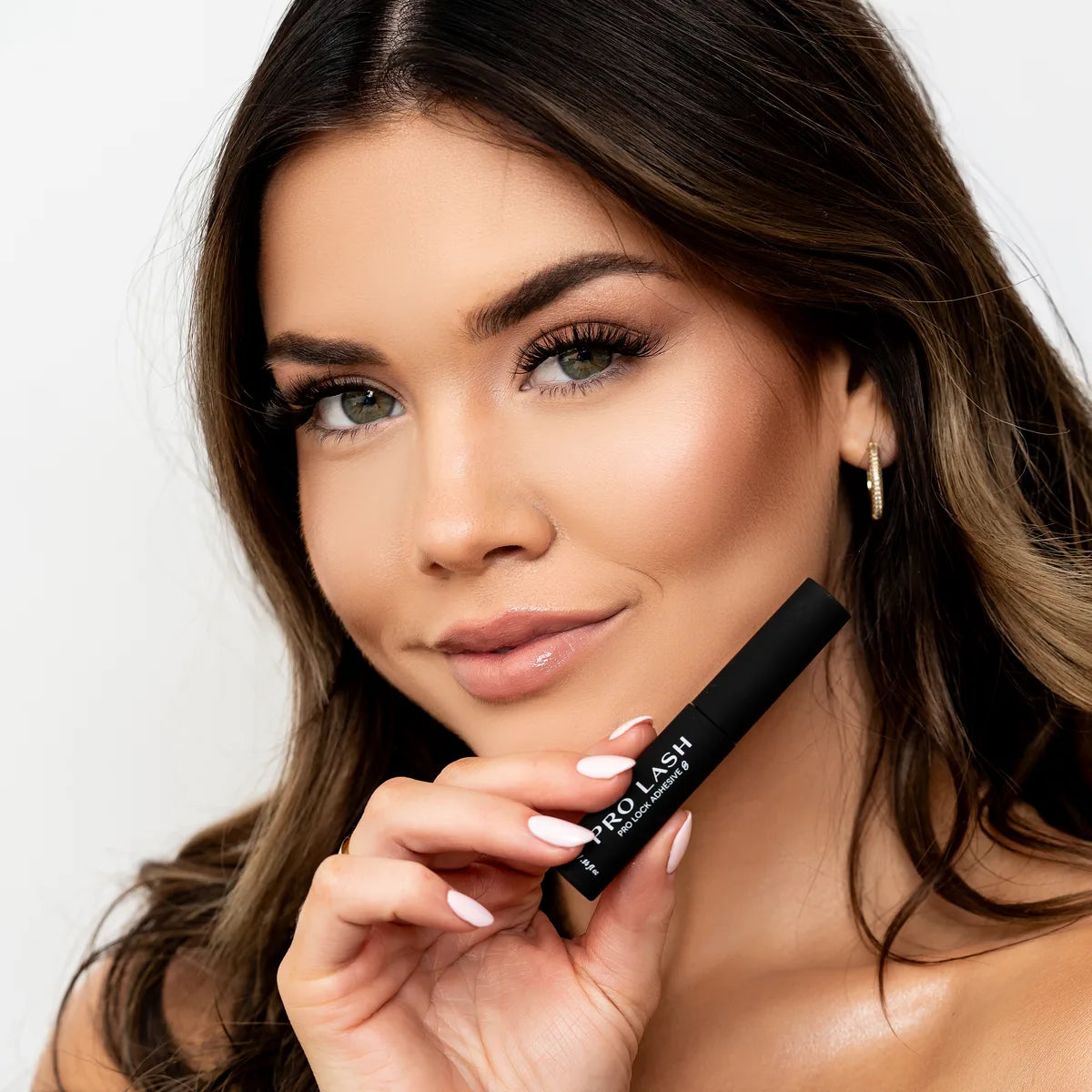 Lash sealer held by woman with voluminous eyelash extensions and flawless makeup for long-lasting lash hold.