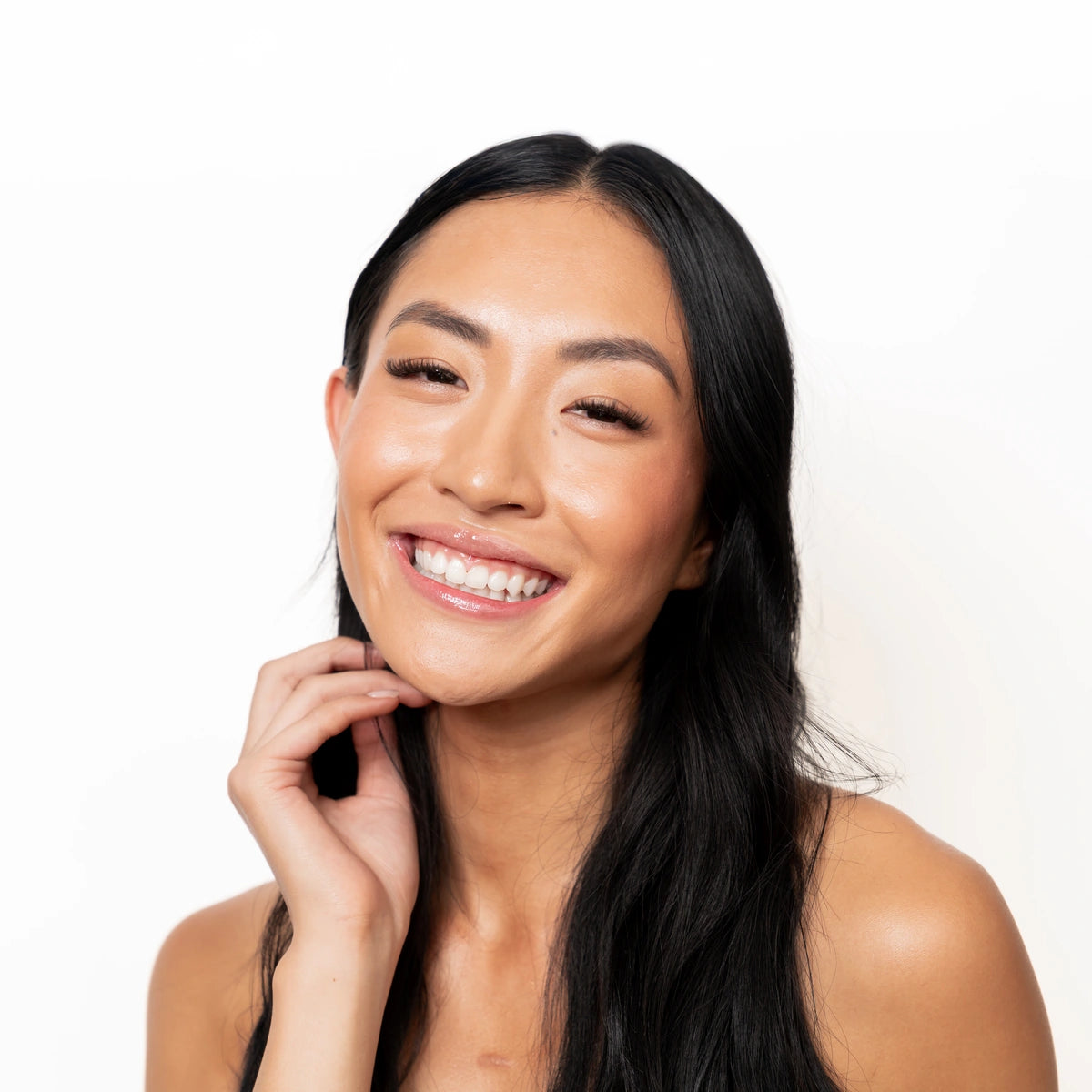 Short volume lash extensions on smiling model with long black hair, showcasing natural glam look and full lash line against white background