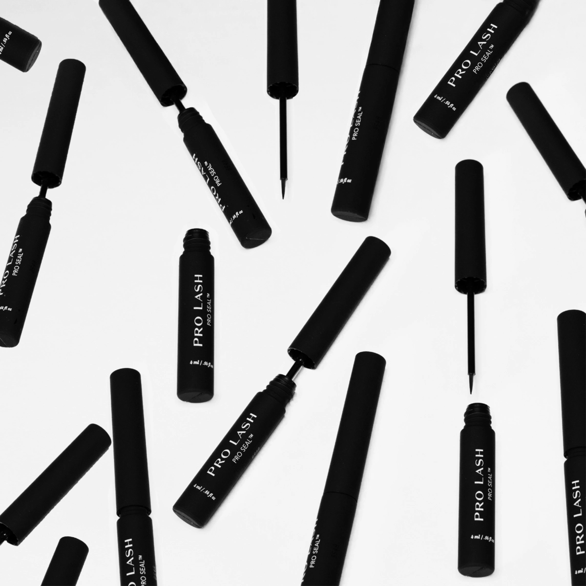 Eyelash extension sealer tubes scattered on white background, showing open and closed Pro Lash Pro Seal applicators in matte black packaging