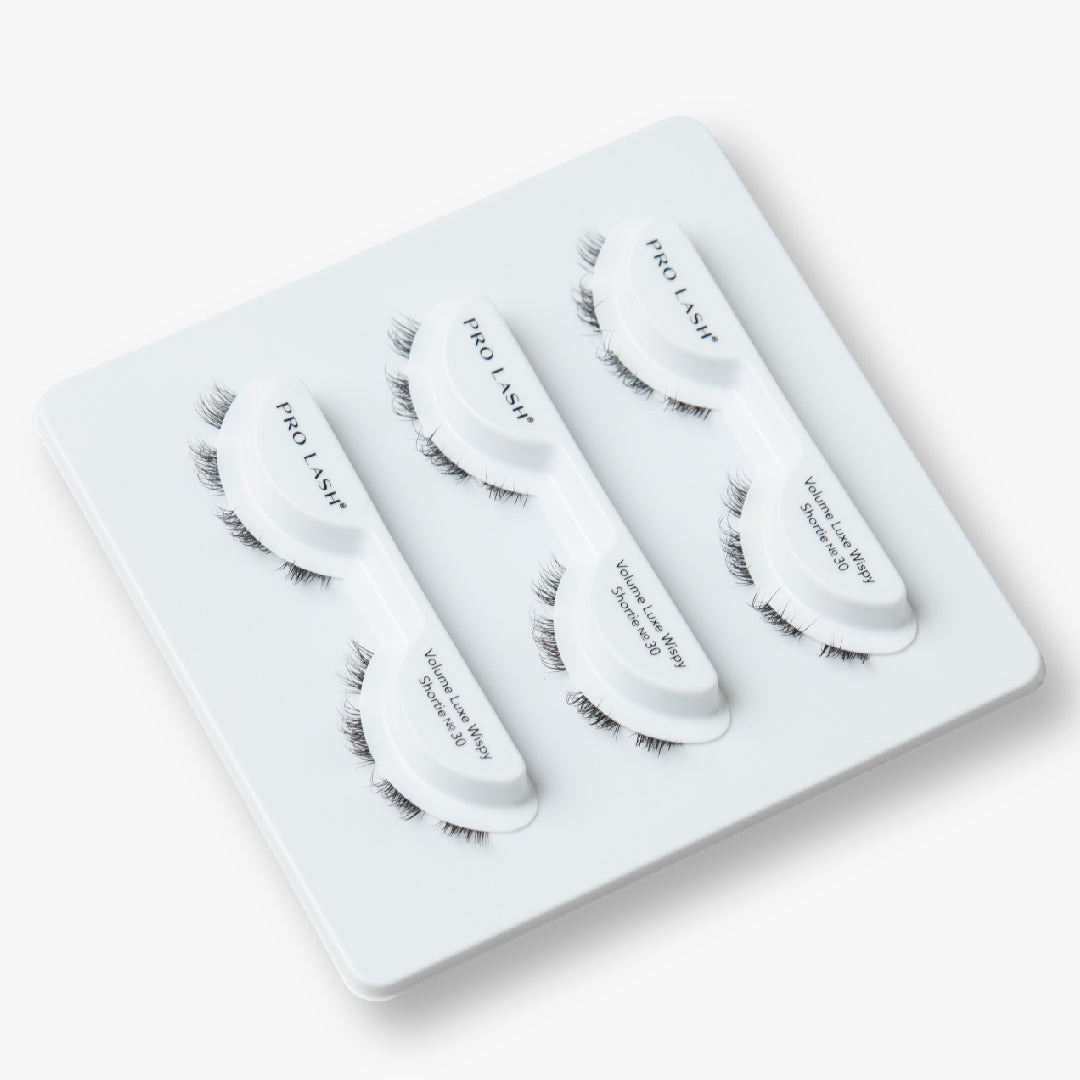Volume wispy lashes in the Luxe Shortie No. 30 style are displayed in three curved trays on a white holder, designed for easy, reusable application.