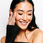 A woman wearing volume wispy lashes with long dark hair and radiant skin smiles with her eyes closed.