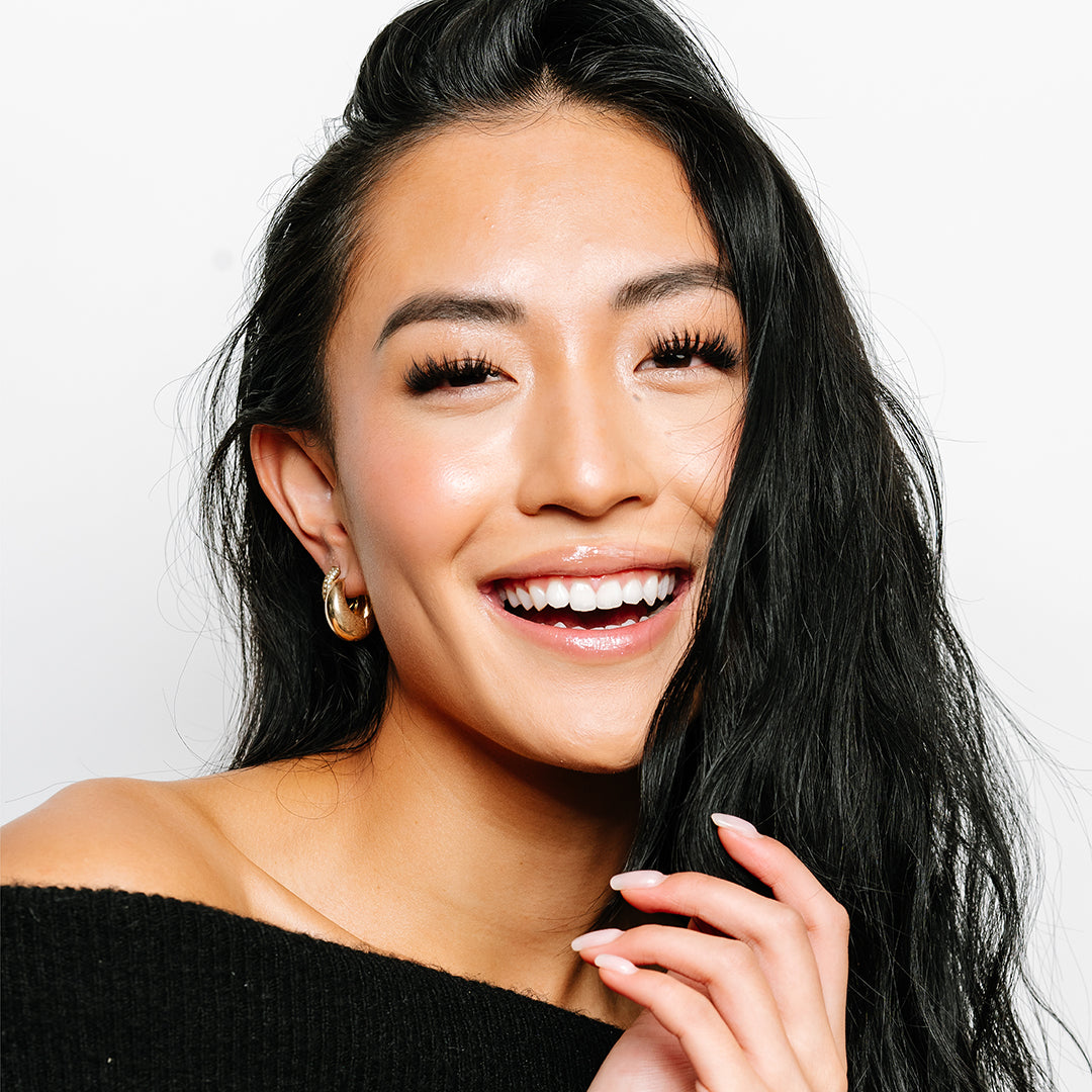 Volume wispy eyelash extensions on smiling woman with long, fluttery lashes and a radiant, natural makeup look.