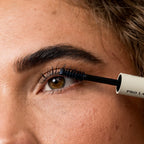 DIY natural eyelash extensions applied with adhesive brush like mascara to upper lashes of a green-brown eye